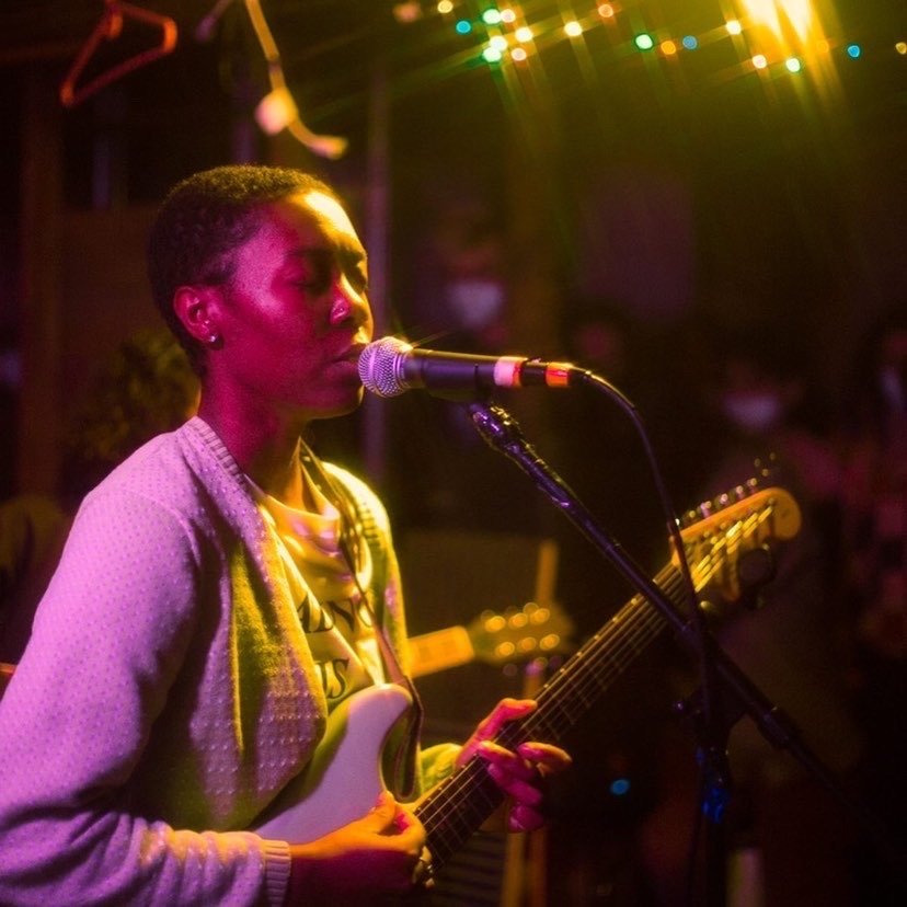 Amore sings peacefully amidst colorful, stringed lights and bare clothes hangers.