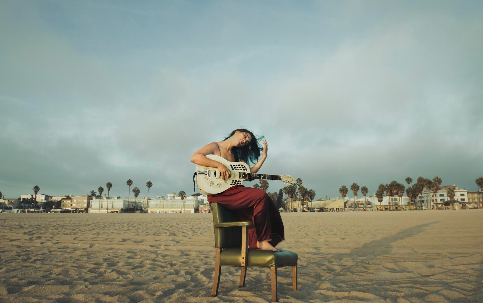   Vane sits atop a vinyl green chair surrounded by sand. She cradles her guitar carefully as she fixes the stray hairs whipping in the salt air’s wind.   